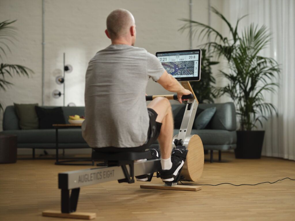 Rear view of a man training on the AUGLETICS rowing machine in a modern living room.