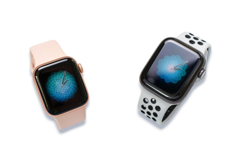 Zwei Smartwatches, eine mit rosa Armband und eine mit weiß-schwarzem Sportarmband, zeigen Aktivitätsanzeigen
