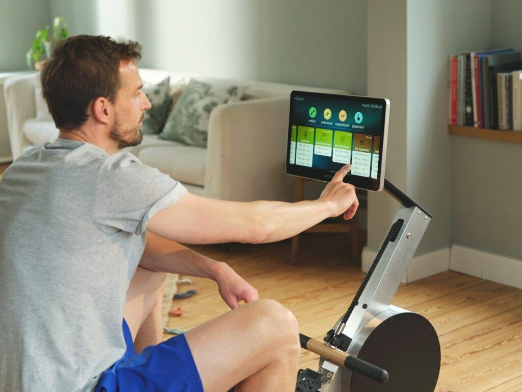 Rudern gegen Übergewicht: Der ideale Weg zu einem gesünderen Körper 5 Mann bedient das Touchscreen-Display eines AUGLETICS Rudergeräts, auf dem verschiedene Trainingsprogramme angezeigt werden.
