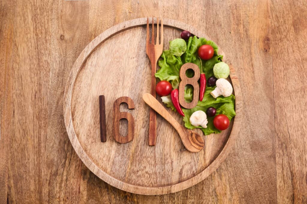 A round wooden plate symbolizes a clock. Intermittent fasting 16:8 – eating window and fasting phase