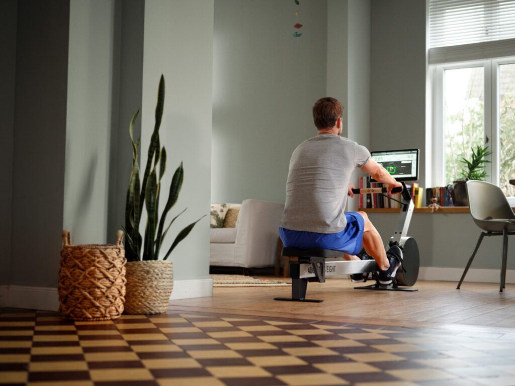 Man trains on a rowing machine in a stylishly furnished living room with plants and cozy decor.
