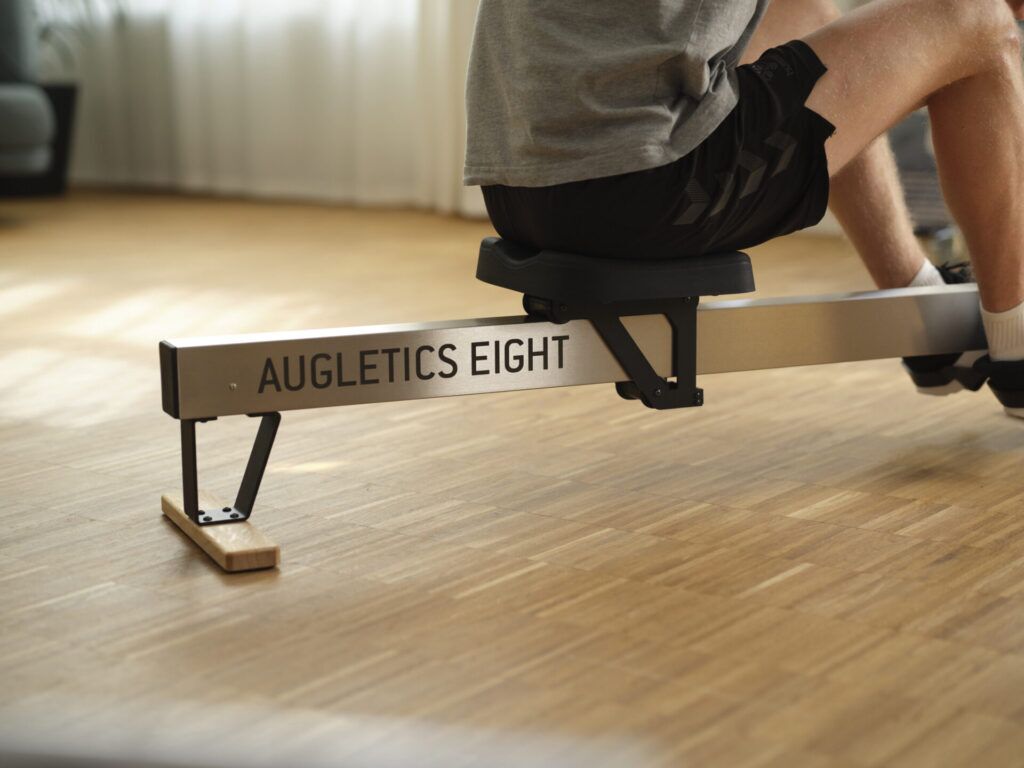 Nahaufnahme des Sitzbereichs eines Augletics Eight Rudergeräts auf einem hellen Holzboden, mit Fokus auf das markante Logo