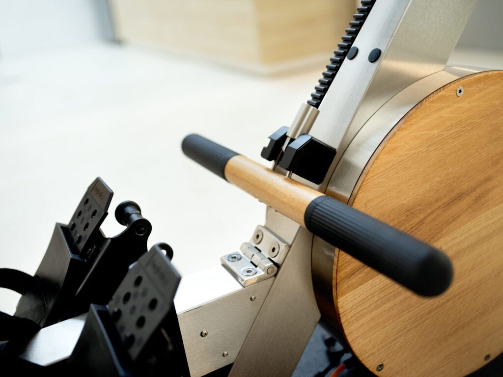 Detailaufnahme der Griffe und Fußstützen eines AUGLETICS Rudergeräts mit Holz- und Metall-Design.